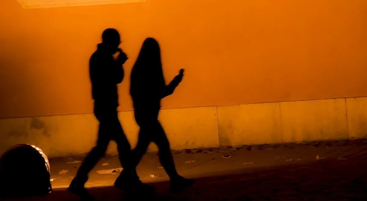 Two evening shadows walking along an orange-lit wall